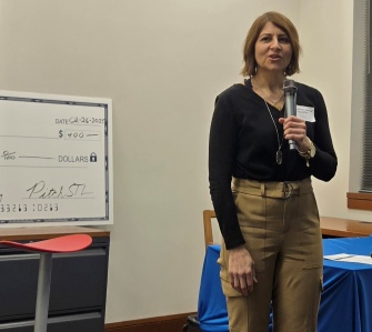 Woman speaking next to large check display.